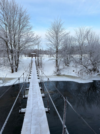 Wooden suspension bridge over a frozen river in the winter forest.