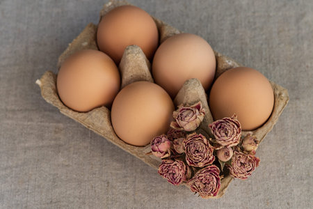 Eggs in a cardboard box with dried roses on a gray background