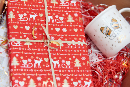 Preparing care package, seasonal gift box with mug and other gifts in red color with christmas ornament. Personalized eco friendly basket for winter holidays. Selective focus.の写真素材