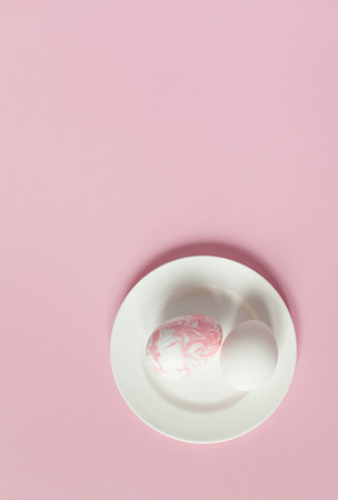 White Easter eggs on white plate on a light pink background, colored decorations, minimalistic design, vertical shotの写真素材