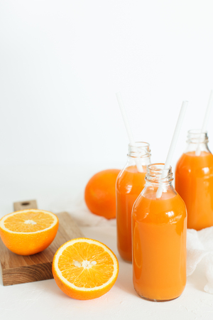 Three bottles of orange juice and tubes are on the table on a white background, as much as two oranges and one orange cut into wooden Boards. Daylight, horizontal image.の写真素材