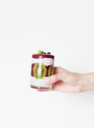 Smoothies in a glass in a hand on a white background with berries and fruits, blueberries, kiwi and chia seeds. Horizontal image, daylight, space for text.の写真素材