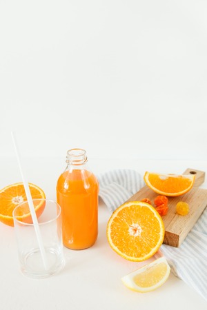 A bottle of orange fresh on a white table, next to a glass of fresh and oranges with lemon. Daylight.の写真素材