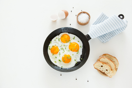 Fried scrambled eggs in a frying pan, bread and salt on a white backgroundの写真素材
