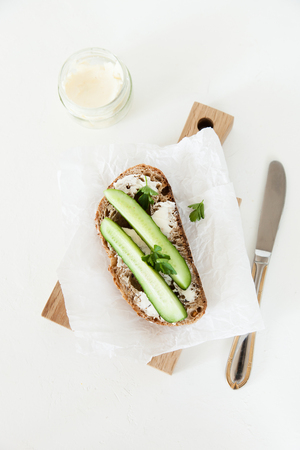 A piece of bread with butter, salt with cucumber and greens lies on a wooden board on a white background. A minimalistic image with space for your text.の写真素材