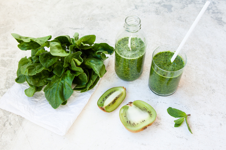 Green cocktail in a bottle and in a glass with spinach, mint, rosemary, kiwi and apple on a light background. Daylight, open space for your text.の写真素材