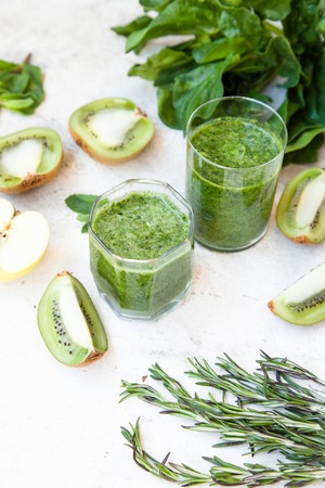 Green cocktail in a bottle and in a glass with spinach, mint, rosemary, kiwi and apple on a light background. Daylight, open space for your text.の写真素材