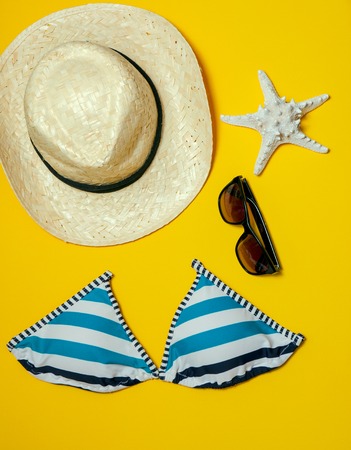 Summer holidays flat lay concept on yellow. Bikini, sunglasses, seashells hat. Vacation concept.の写真素材