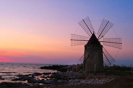 Windmill on the shore seaside with sunset in the background. North of Sicily, Trapani, old fashioned windmill on the coastの写真素材
