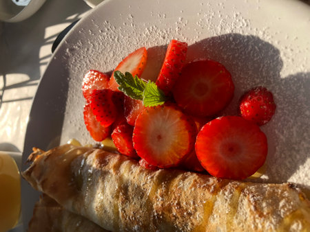 breakfast pancakes on the plate with fresh strawberries in the morning sunlightの写真素材