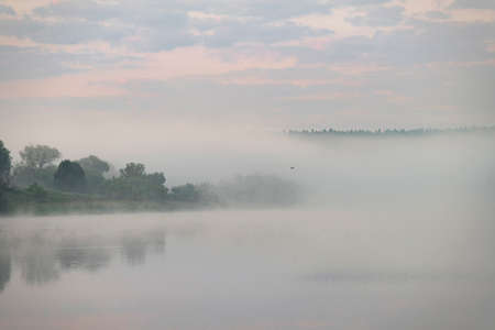 Fog is curling over the grassed river banks at dawn, Oka river, Kaluga region, Russiaの写真素材