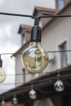 Photo of cozy electric bulbs in the garden over the old tile roof in the city.の写真素材