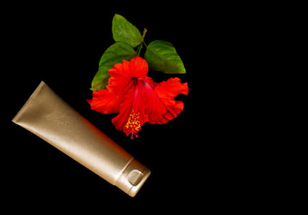 Golden cream bottle and tropical flower on the black background. Product for skin care concept.