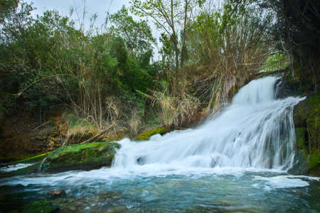 A beautiful waterfall in a forest with blue water and trees.の写真素材