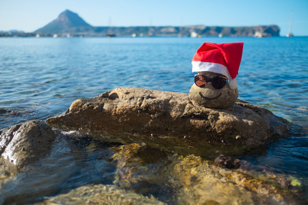 Stone with a smile and in a Santa red hat is laying on a big rock.の写真素材