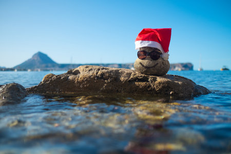 Stone with a smile and in a Santa red hat is laying on a big rock.の写真素材