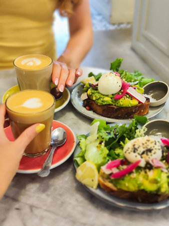 Female hands is holding a coffee cups. Coffee and a breakfast is on the table.の写真素材