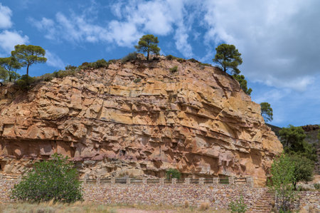 Rugged rock cliff with layers of exposed stone under a bright blue sky.の写真素材
