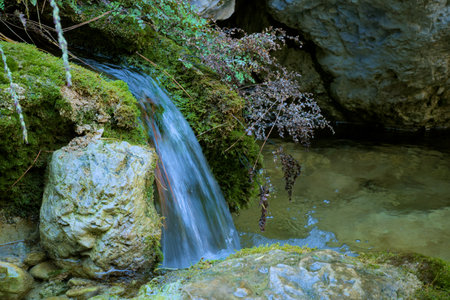 Serene waterfall cascading over moss-covered rocks into a clear.の写真素材