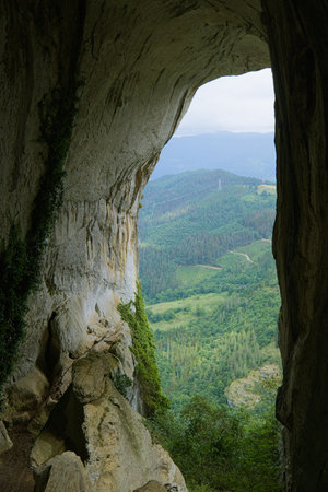 A stunning view from inside a cave overlooking lush green hills and forests in the north of Spain.の写真素材