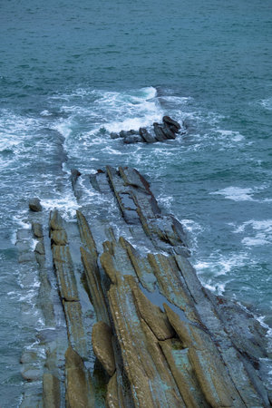 Layered rock formations emerging from the ocean along the rugged coastline in the north.の写真素材