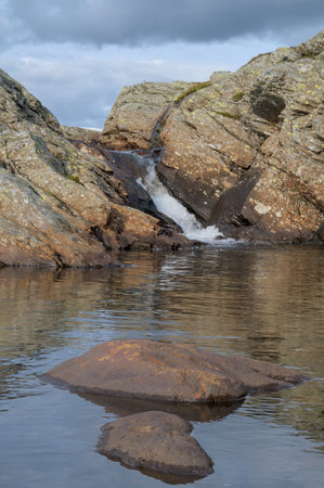 A serene photo of a small waterfall flowing between rocky cliffs into a calm pool.の写真素材