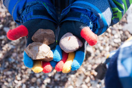 A boy in multi-colored gloves holds three stones.の写真素材