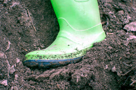 Boy's feet in dirty rubber boots. Leisure for children in the village. The boy is standing in the...