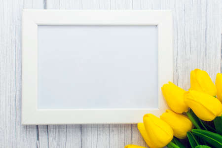 Mockup of picture frame decorated yellow tulip flowers on wooden background. Styled stock photography.の写真素材