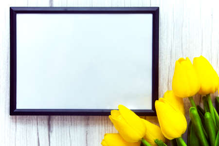 Mockup of picture frame decorated yellow tulip flowers on wooden background. Styled stock photography.の写真素材