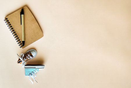 A pair of sports sneakers on a beige background lie next to a notebook and a pen