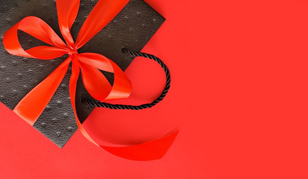 Black bag with a red bow on a red background with space for textの写真素材