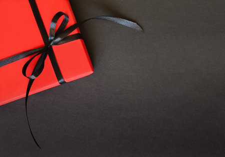 Red gift box with a black bow on a black background with space for textの写真素材
