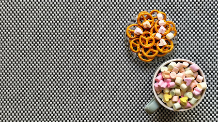A bowl of marshmallows and pretzels on a gray background. Space for text, top view.の写真素材