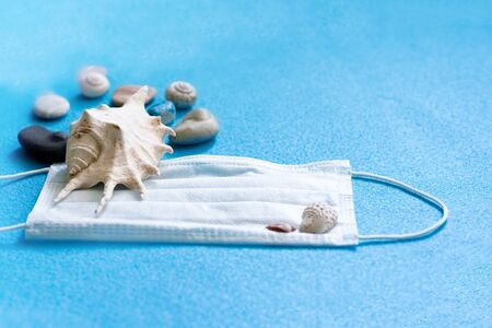 Medical face mask and shells on a blue background. Tourism crisisの写真素材