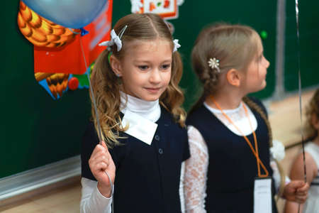 Beautiful girl first grader in school uniform sitting at a desk in classroom. Schoolgirl in school uniform, Knowledge Day. September 1. High quality photoのeditorial素材