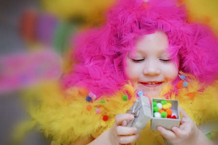 A little girl lies in a blurred festive setting. Feathers, confetti, gift. Birthday, holiday. High...