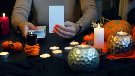 Blurred Fortune teller of hands holding blank card and tarot cards on table near burning candles in candle light. Forecasting concept. ... High quality photoのeditorial素材