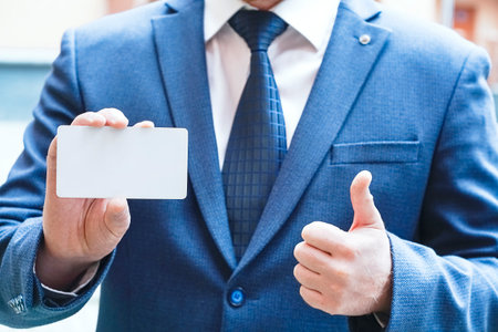 A man holds in his hand a blank white card and shows a class sign. High quality photoの写真素材