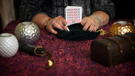 Fortune teller of hands holding tarot cards on table near burning candles in candle light. Tarot cards spread on table. Forecasting concept.のeditorial素材
