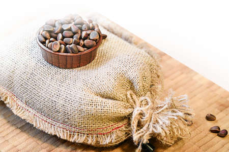 unpeeled cedar nuts in burlap sack with heap of kernels in wooden scoop and pine cone isolated on white background Cedar cone.の写真素材