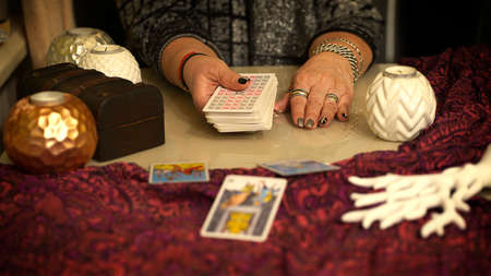 Fortune teller of hands holding tarot cards on table near burning candles in candle light. Tarot cards spread on table. Forecasting concept.のeditorial素材
