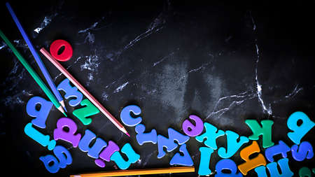 Black blackboard background with coloful letters of the english alphabet. Flat lay supplies with...