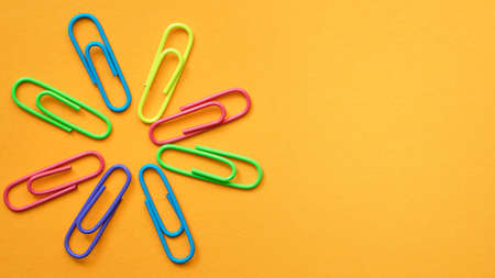 Multicolored paper clips in a circle in the form of a flower on the blank Orange background. High quality photoの写真素材