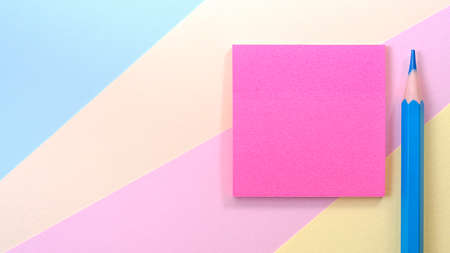 A pink square blank piece of paper lies on a multi-colored background, next to it lies a blue pencil. High quality photoの写真素材