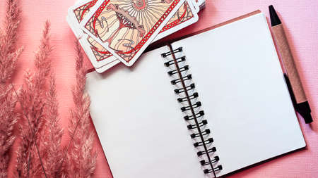 Moscow, Russia - June 2021: View of Golden tarot cards with notebook pink background, esoteric...