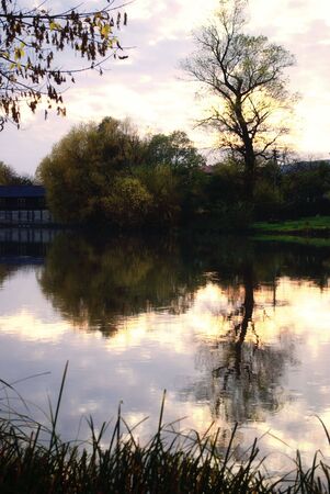 Sundown on river in autumn, dramatic slouds on the and reflection