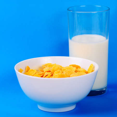 Breakfast from milk in glass and cornflakes over blue background