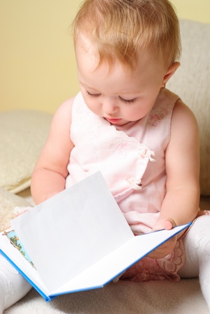 Little girl reading a book, sitting on the sofaの写真素材