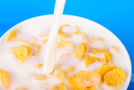 Breakfast from pouring milk and cornflakes over blue background